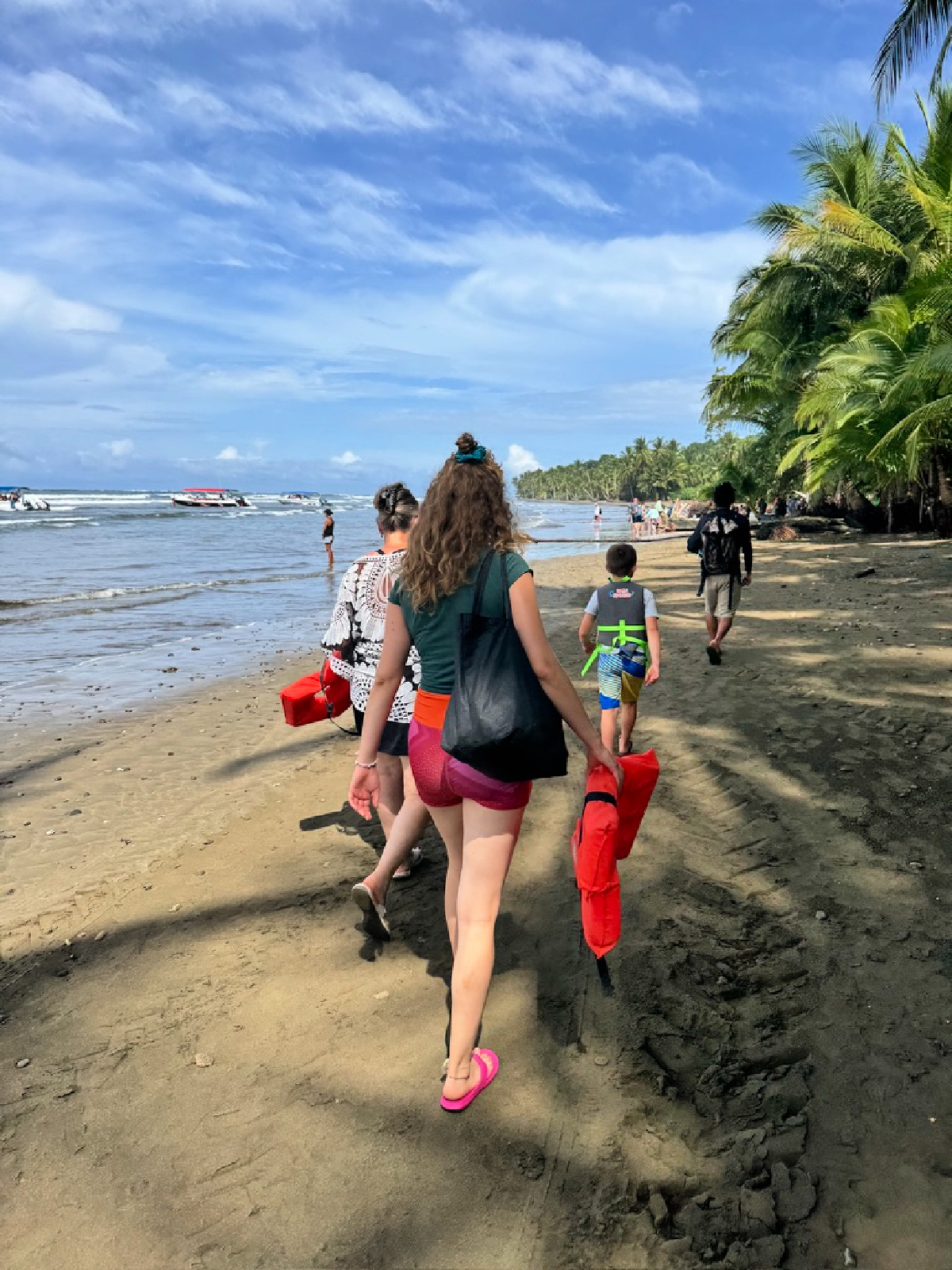 People walking along a tropical beach in Costa Rica carrying life jackets near the shoreline.