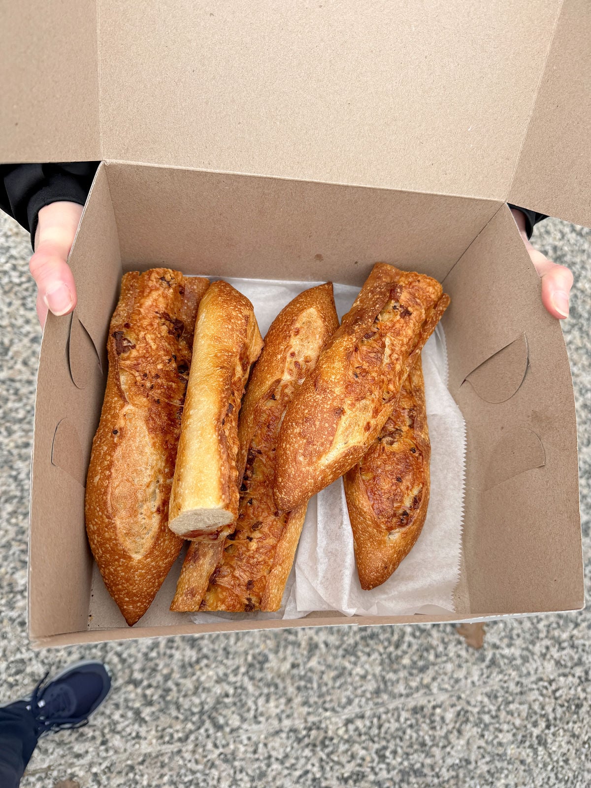 Bacon lardons baked on sliced baguette pieces in a cardboard takeout box from a Pittsburgh food tour.