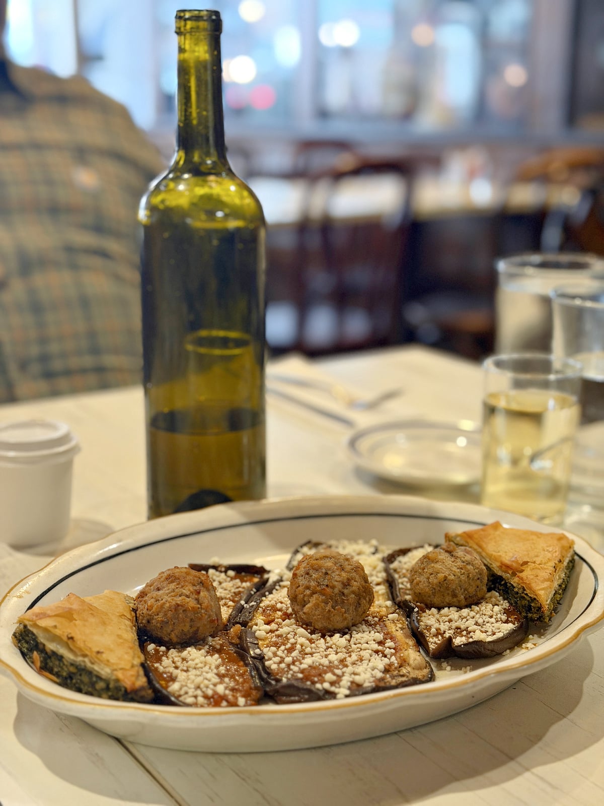 Greek sampler plate with eggplant, meatballs, feta cheese, and spanakopita on a restaurant table.
