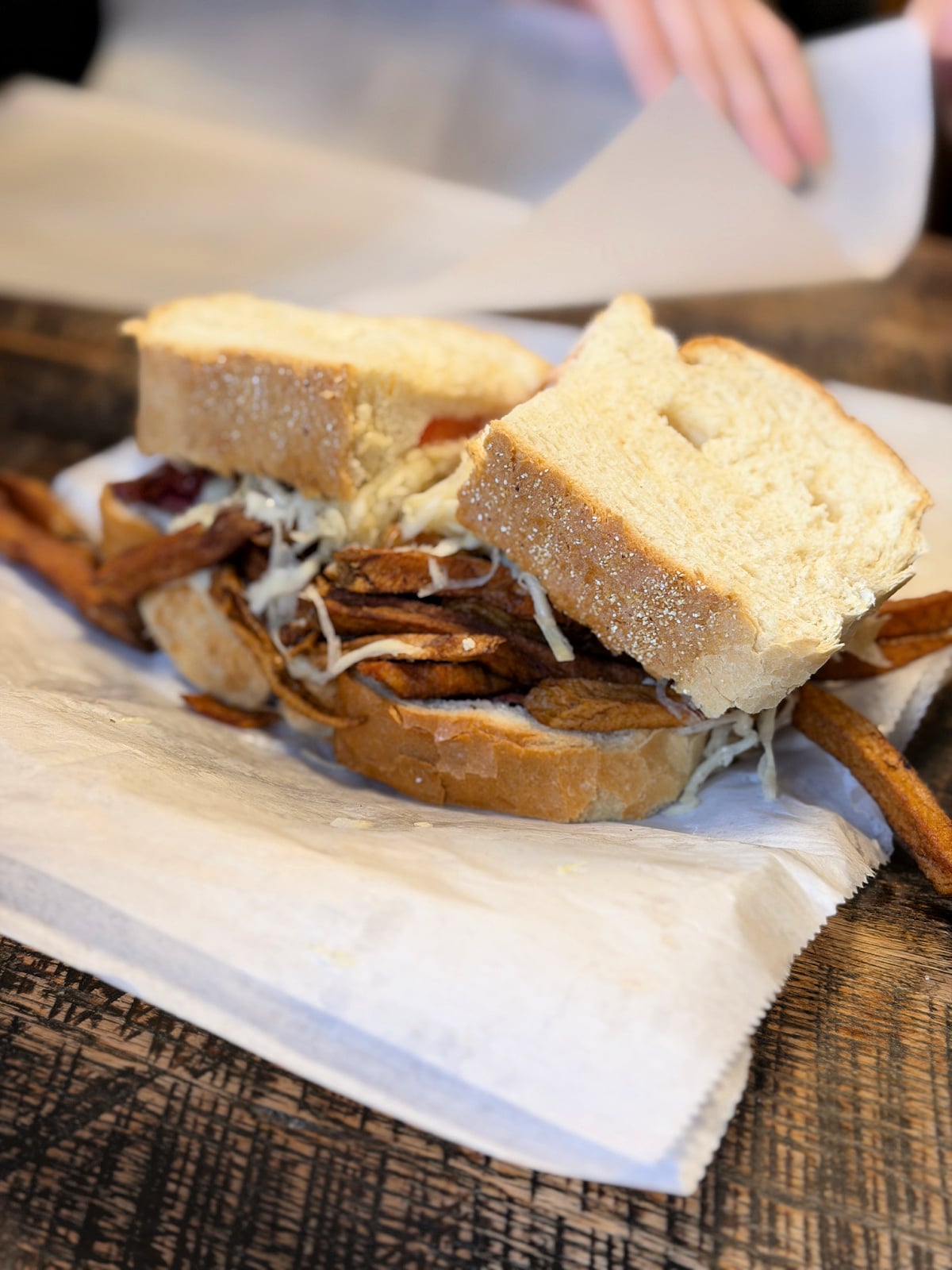 Primanti Bros sandwich with fries and coleslaw inside thick Italian bread on a wooden table.
