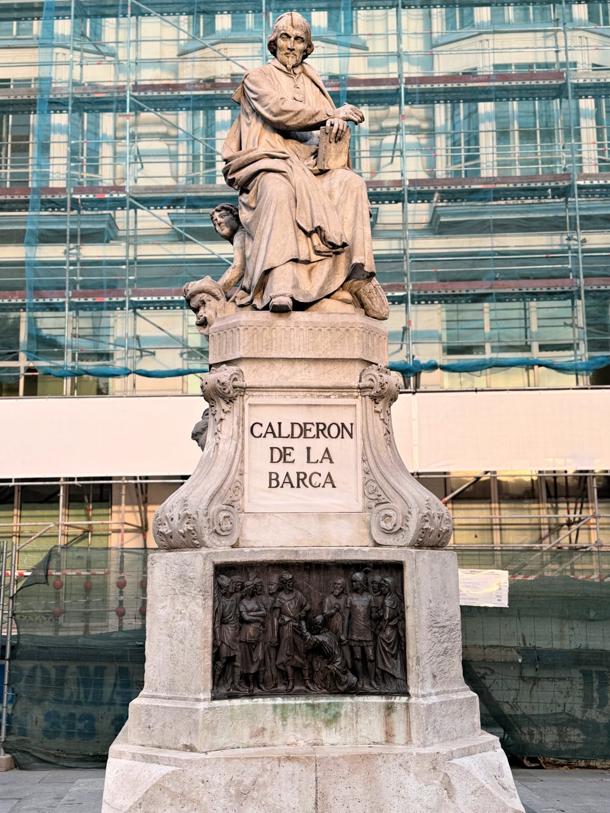 Statue of Calderón de la Barca standing in front of a building covered in scaffolding in Madrid.