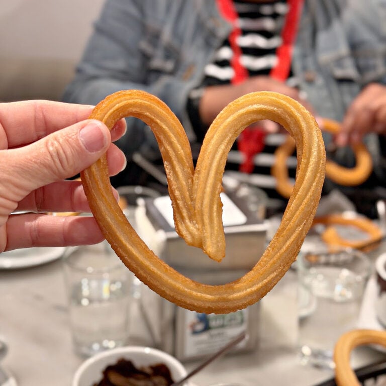 Heart-shaped churro held above a café table during a churros and chocolate stop in Madrid.