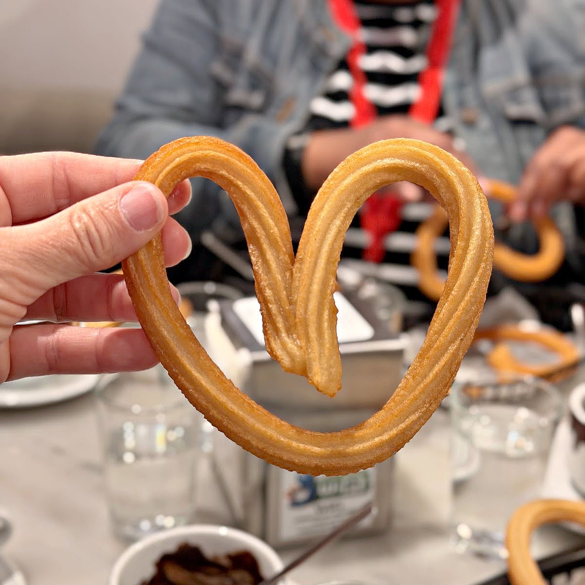 Heart-shaped churro held above a café table during a churros and chocolate stop in Madrid.