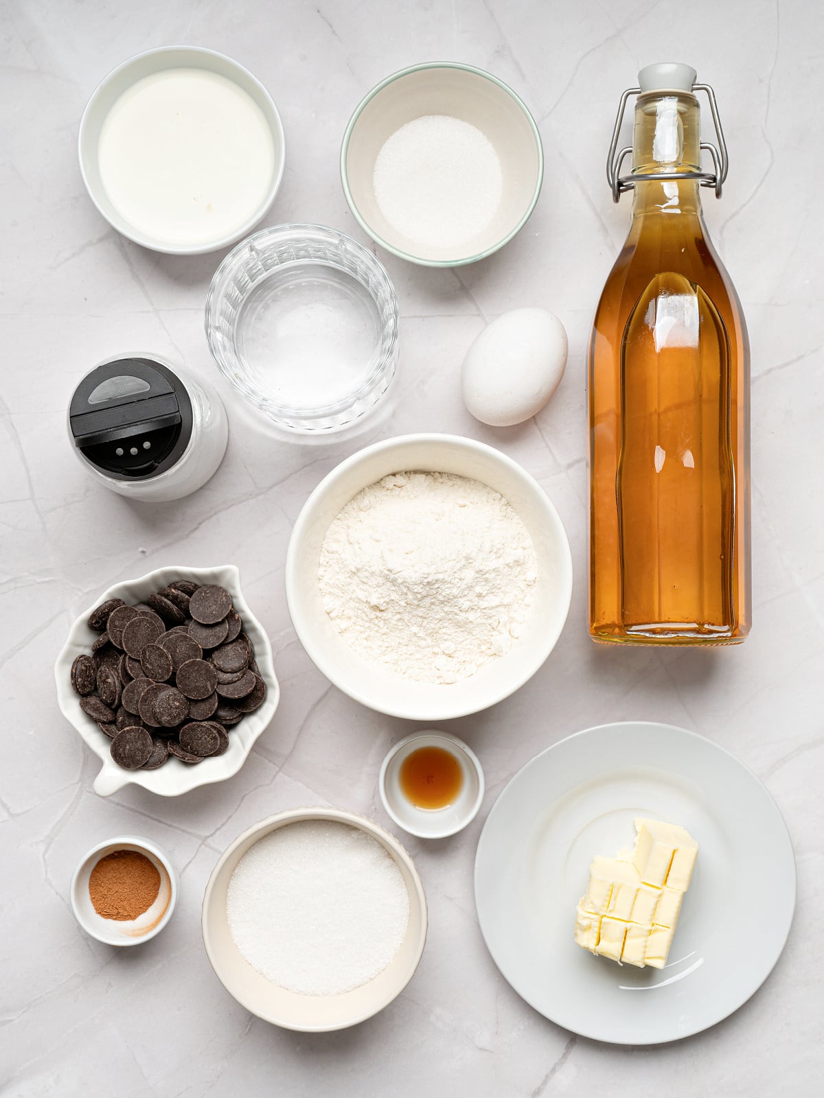 Ingredients for homemade churros and chocolate sauce arranged on a countertop, including flour, butter, sugar, chocolate chips, egg, vanilla, and oil.