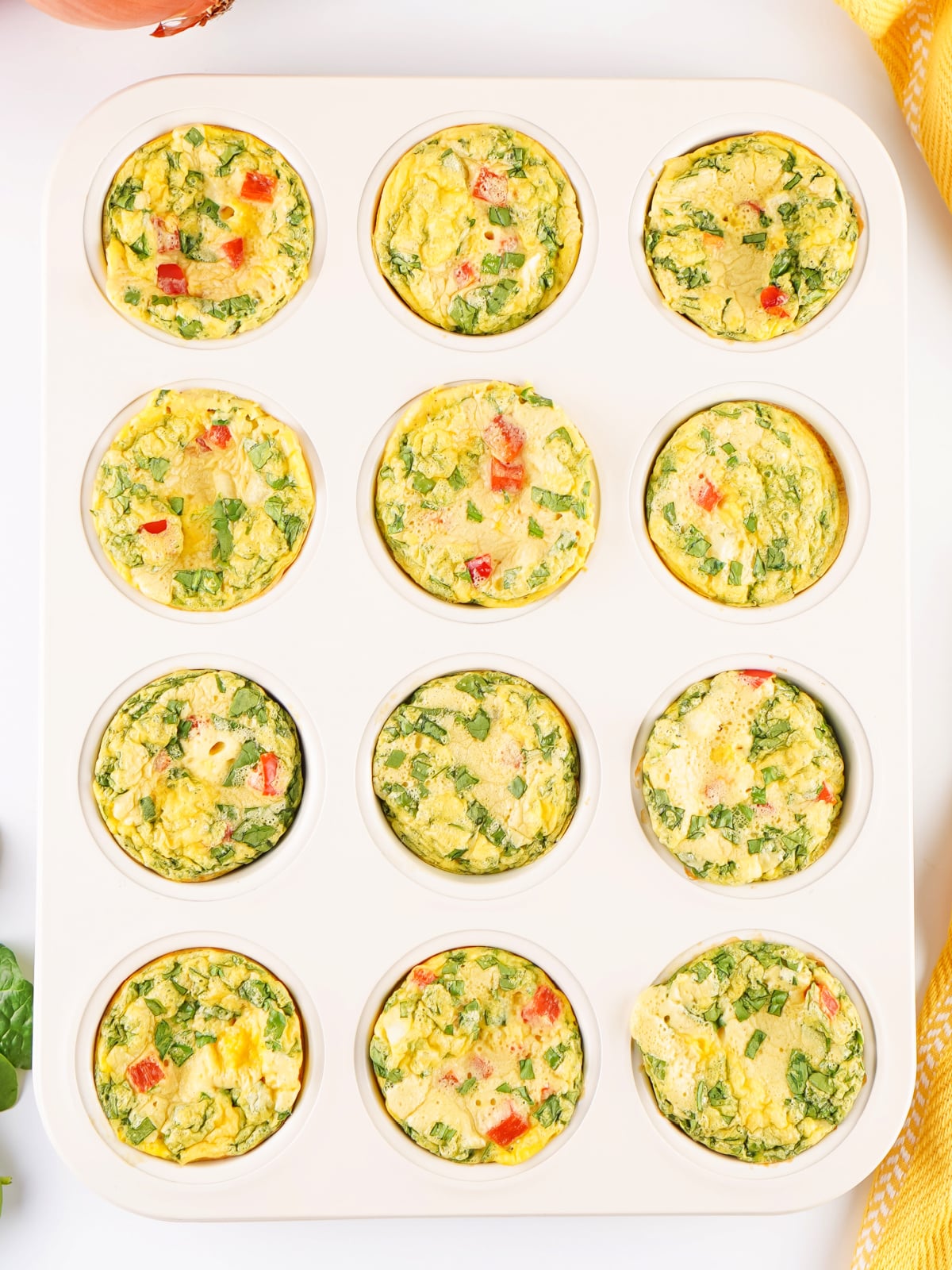Freshly baked egg bites in a silicone muffin pan, filled with spinach, red bell pepper, and cheese.