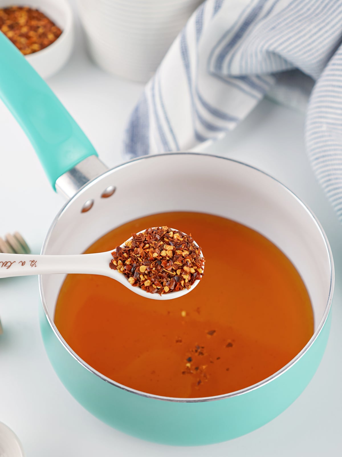 Red pepper flakes being added to warm honey in a saucepan while making homemade hot honey.