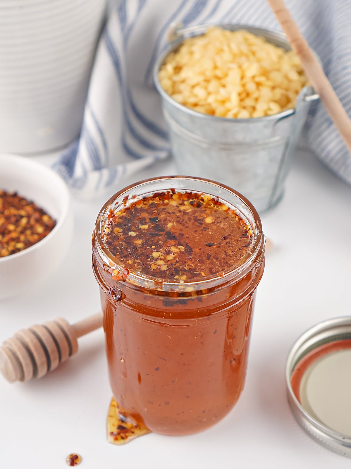 Jar of homemade hot honey infused with red pepper flakes, surrounded by honey dippers and chili flakes.
