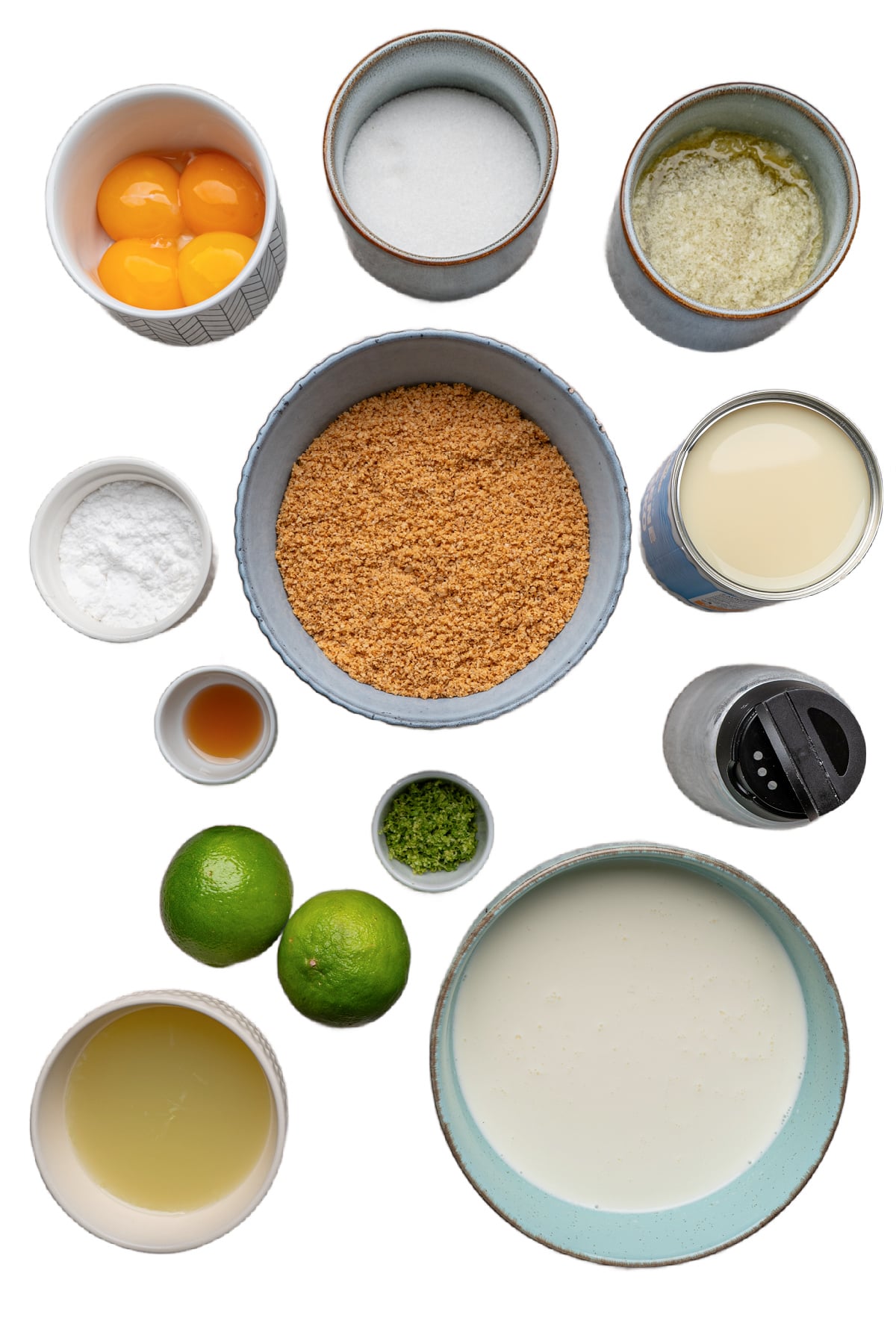 Ingredients for key lime tart arranged on a white background, including lime juice, limes, egg yolks, sweetened condensed milk, cream, sugar, and graham cracker crumbs.