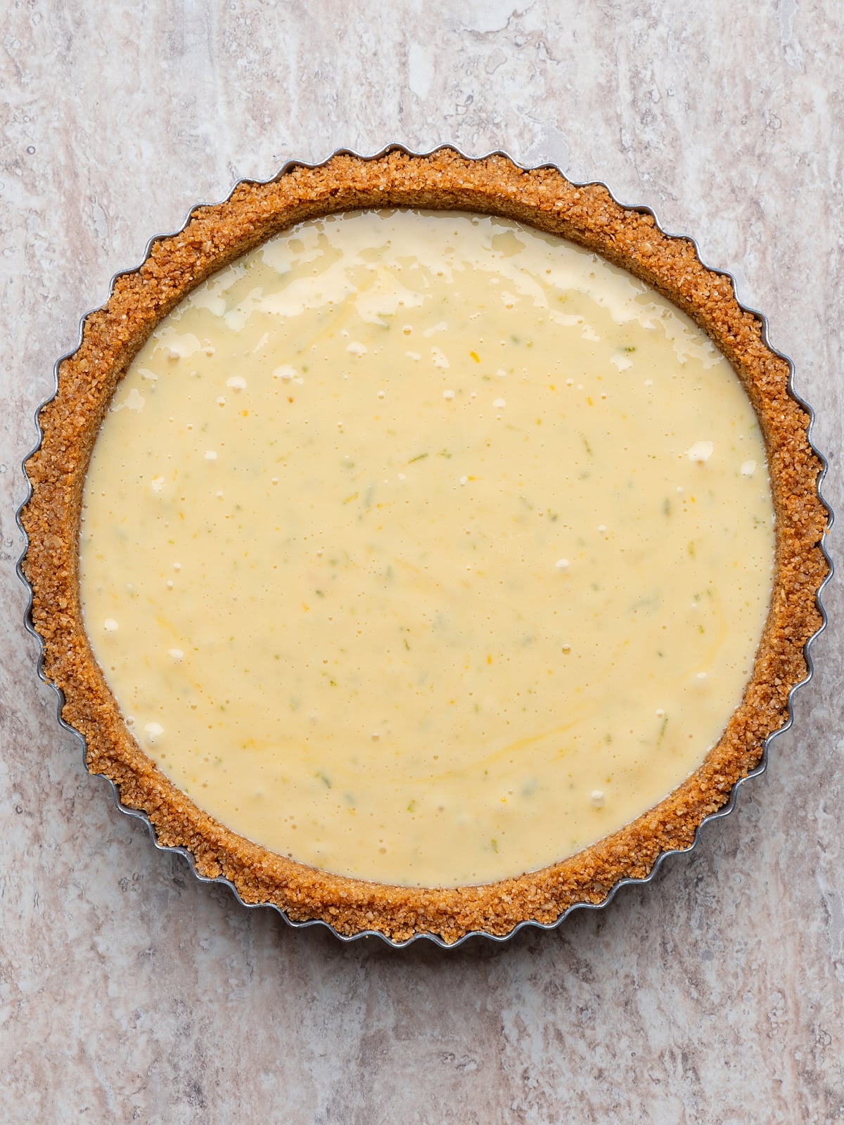 Key lime filling poured into a prepared graham cracker tart crust, ready for baking.