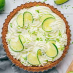 Finished key lime tart decorated with whipped cream, lime slices, and fresh lime zest in a fluted tart pan.