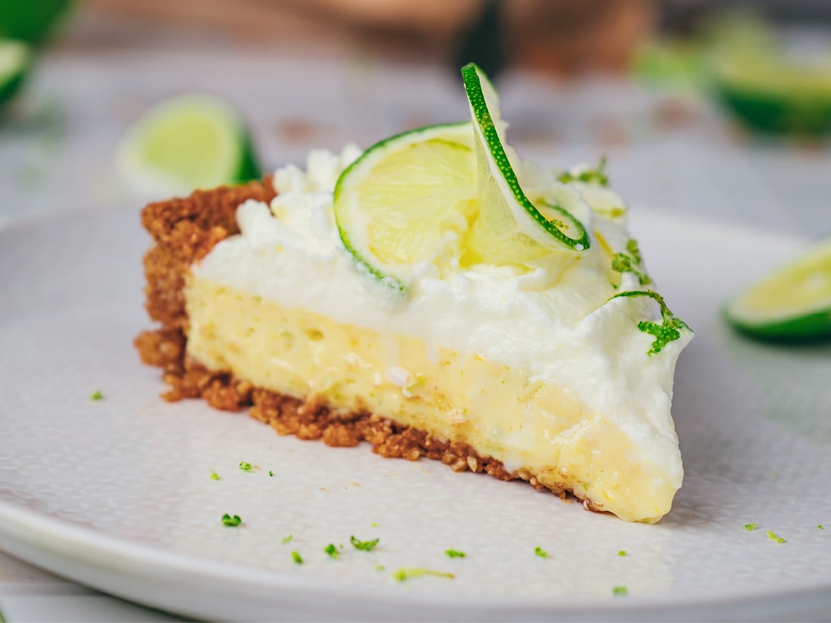 Slice of key lime tart on a plate topped with whipped cream and lime slices.