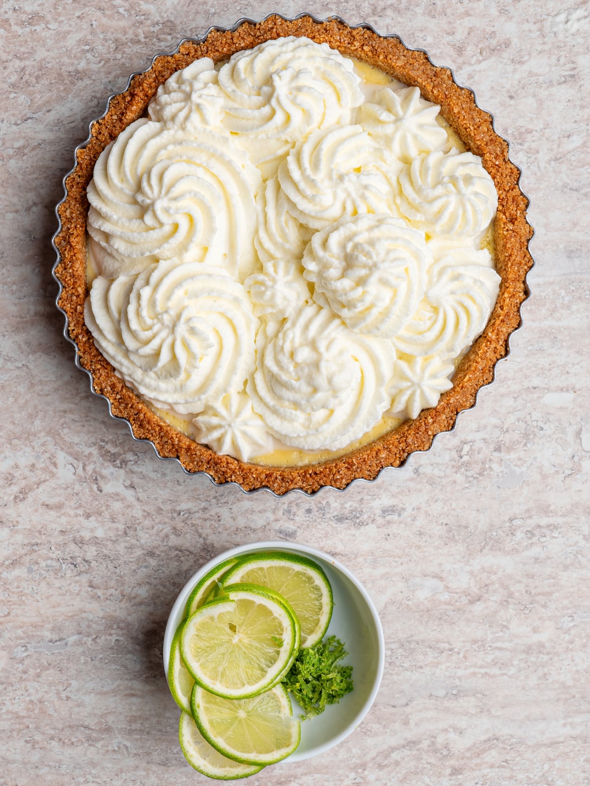 Key lime tart topped with decorative whipped cream swirls before adding lime garnish.