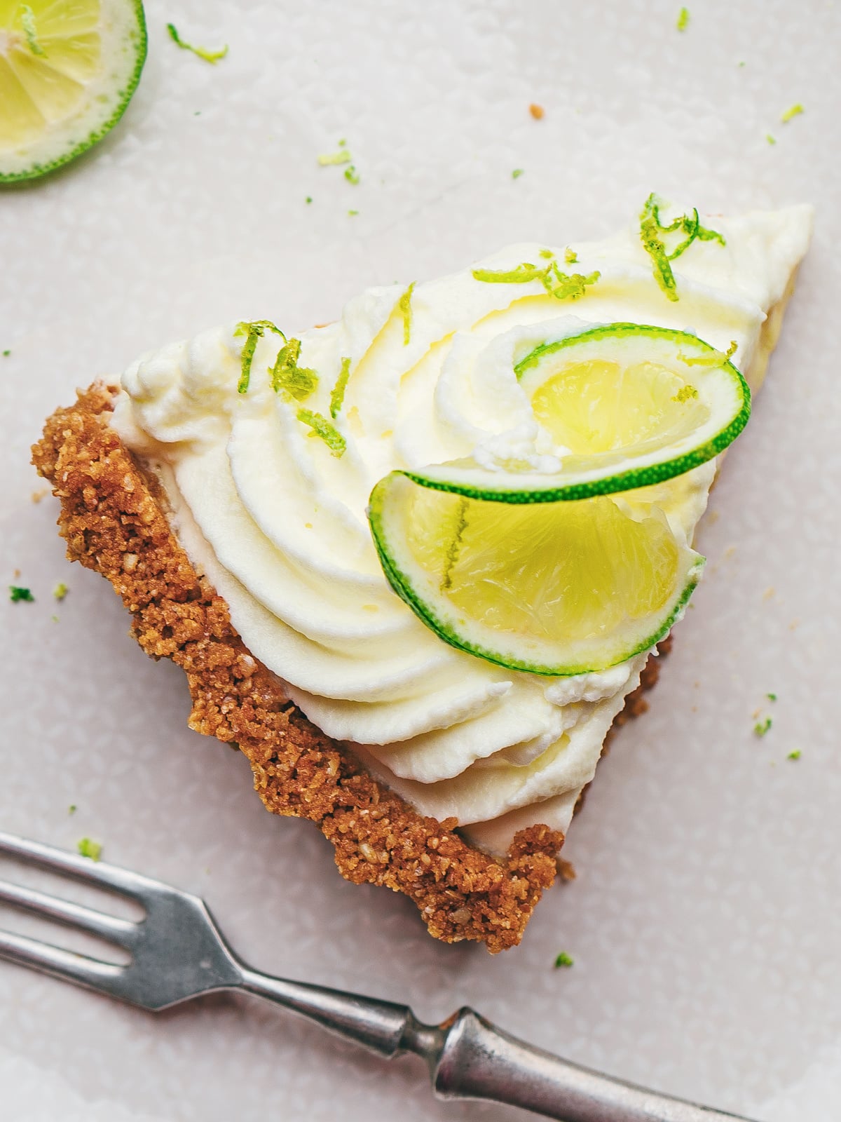 Overhead view of key lime tart garnished with whipped cream swirls, lime slices, and lime zest.