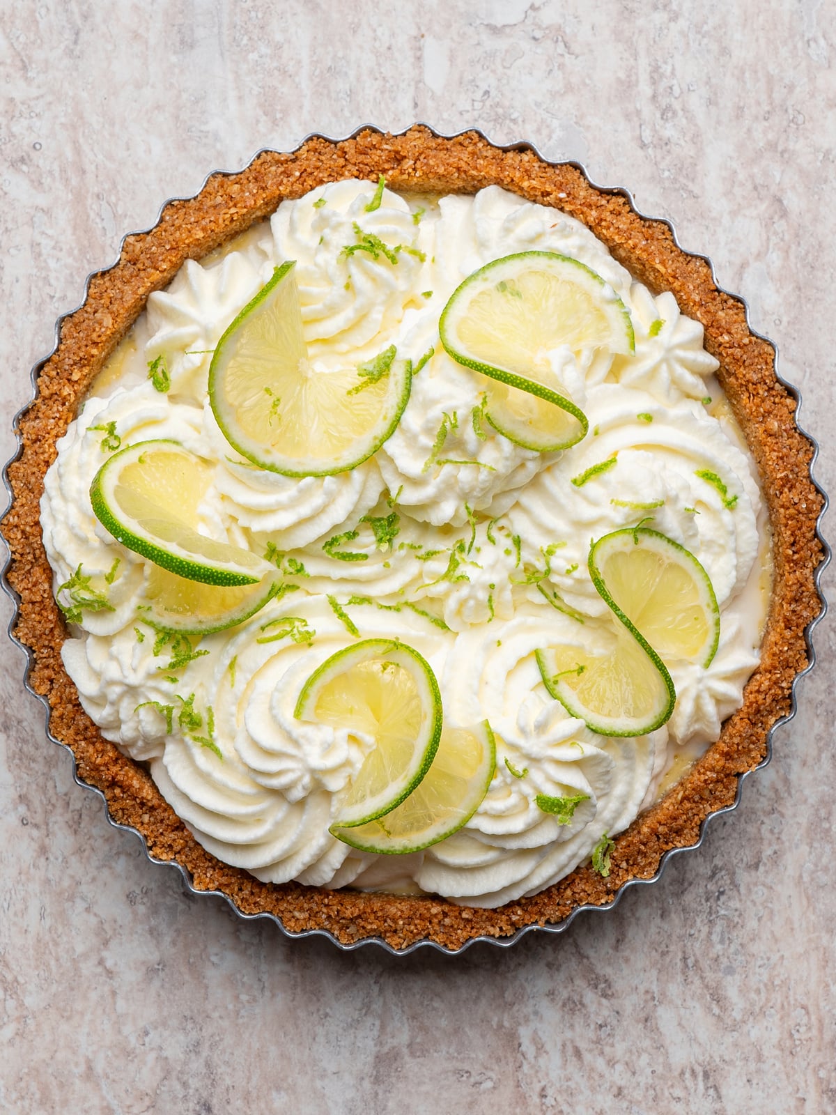 Finished key lime tart topped with whipped cream, lime slices, and fresh lime zest.