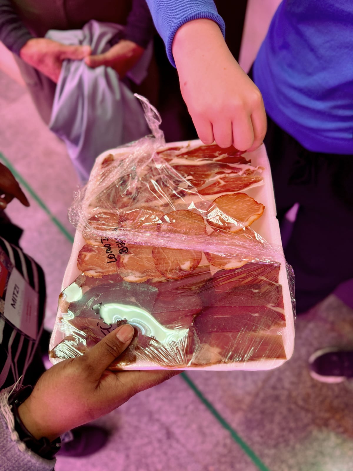 Assorted cured meats and jamón samples wrapped on trays at a Spanish market stall.
