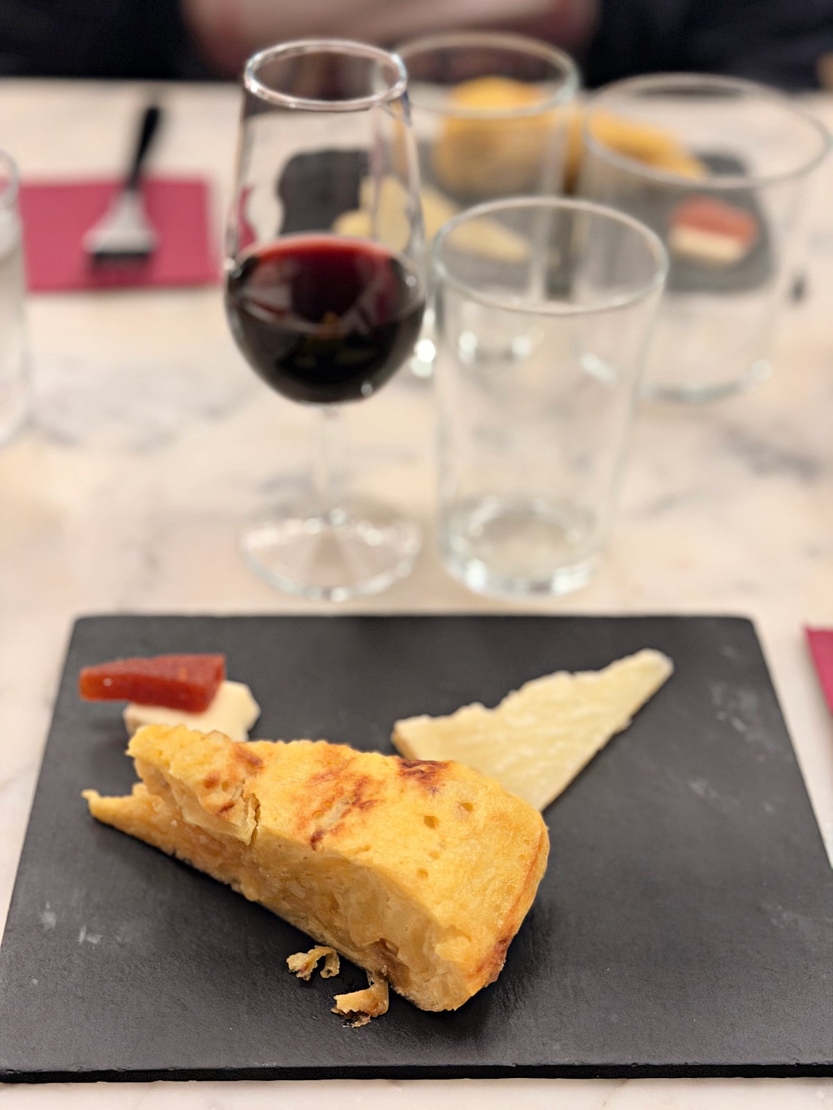 Slice of Spanish tortilla served with cheese, quince paste, and red wine during a tasting experience.