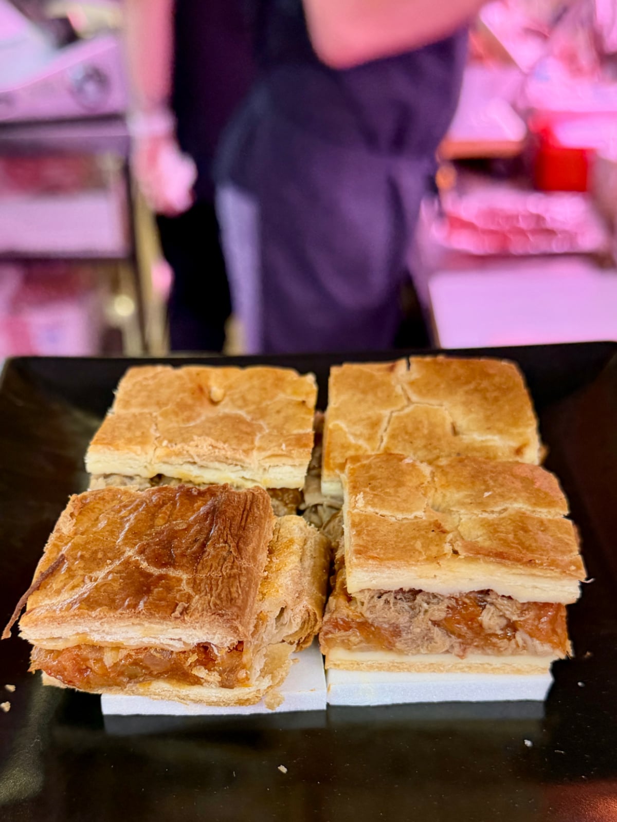 Assorted Spanish empanadas cut into squares and displayed for sampling at a bakery.