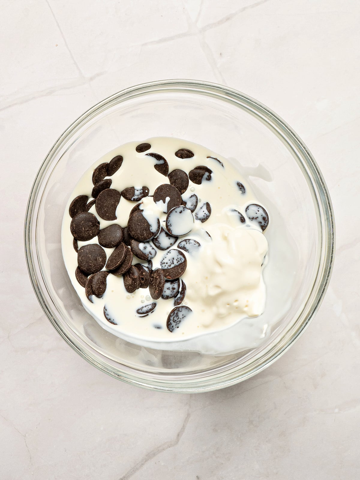 Chocolate chips and heavy cream in a glass bowl ready to be melted into homemade chocolate dipping sauce for churros.