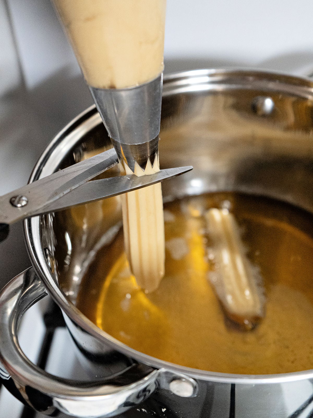 Churro dough being piped into hot oil with a star tip and cut with kitchen scissors before frying.