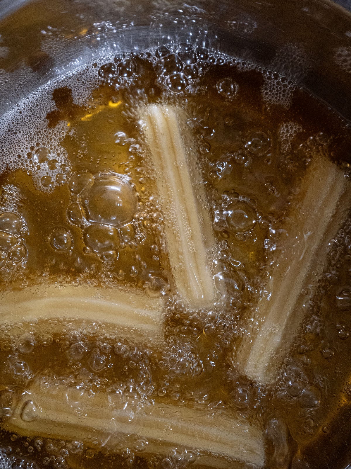 Homemade churros frying in hot oil until golden brown and crispy.