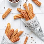 Homemade churros coated in cinnamon sugar served in paper cones with chocolate dipping sauce.