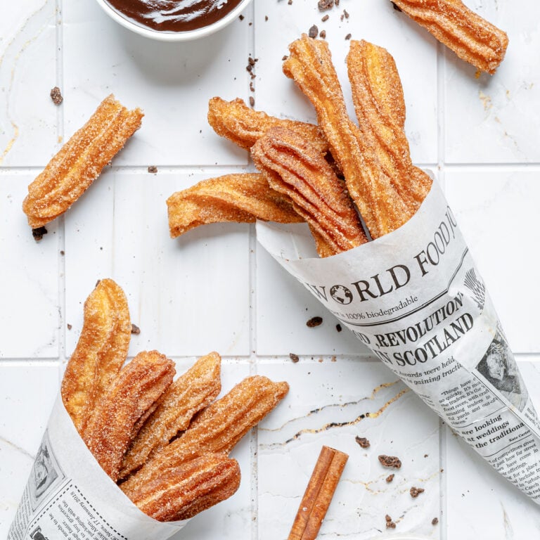 Homemade churros coated in cinnamon sugar served in paper cones with chocolate dipping sauce.