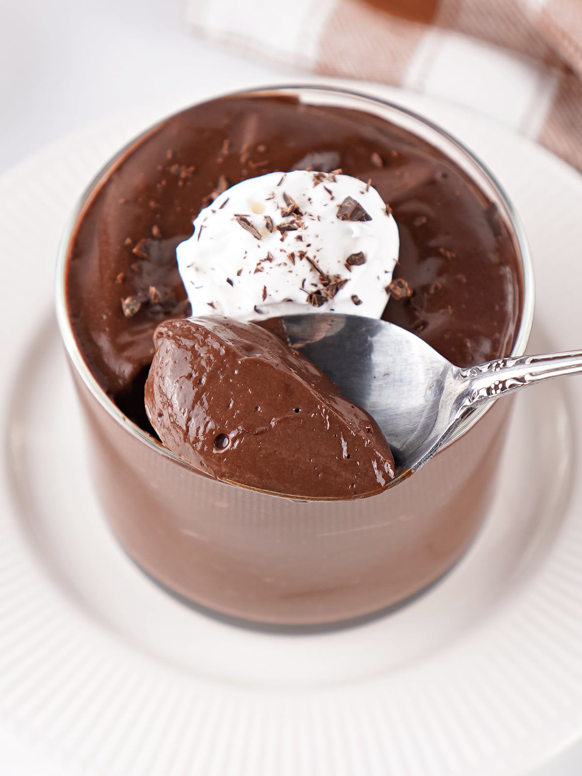 Spoon lifting a creamy bite of chocolate hard-boiled egg pudding topped with whipped cream and chocolate shavings.