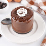 Creamy chocolate hard-boiled egg pudding topped with whipped cream and chocolate shavings in a glass dessert cup on a white plate.