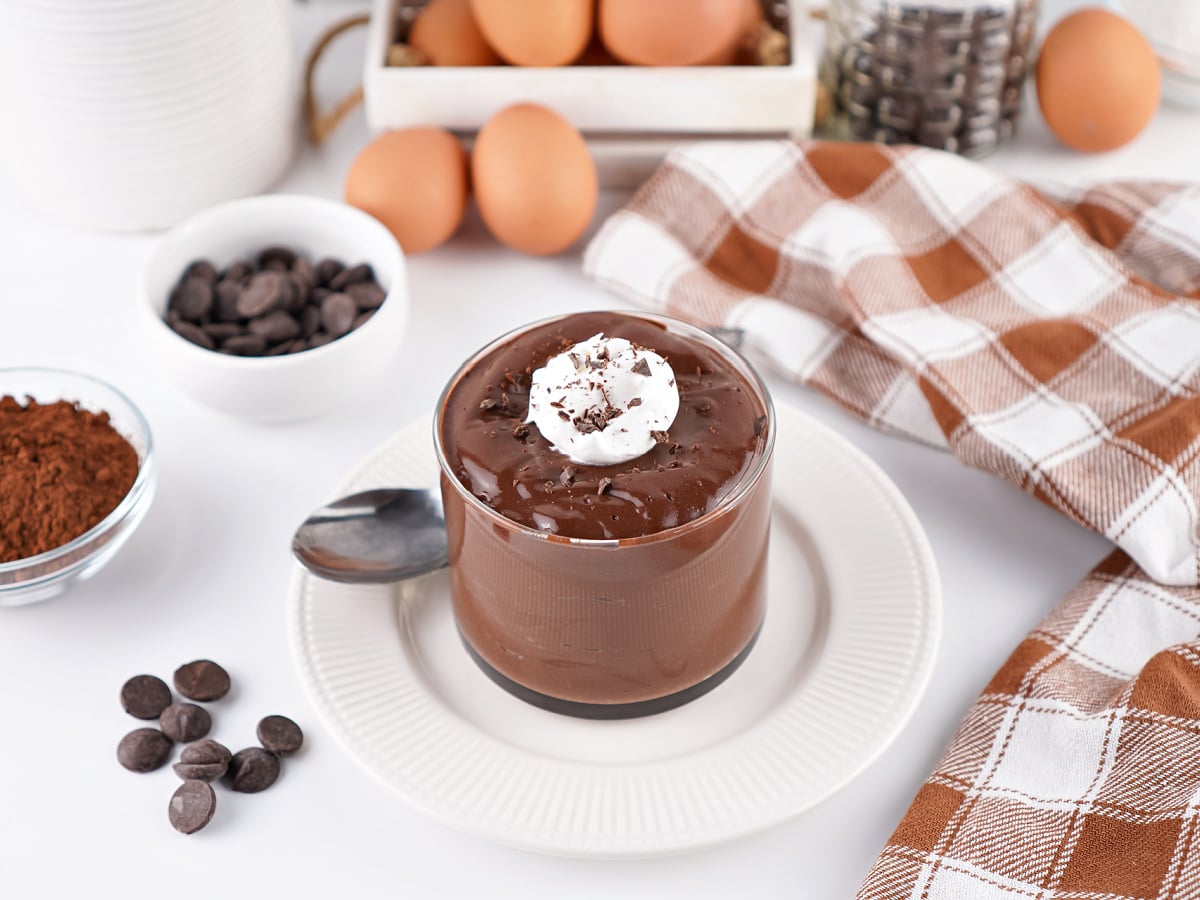 hocolate hard-boiled egg pudding garnished with whipped cream and chocolate shavings, surrounded by ingredients and styling props.