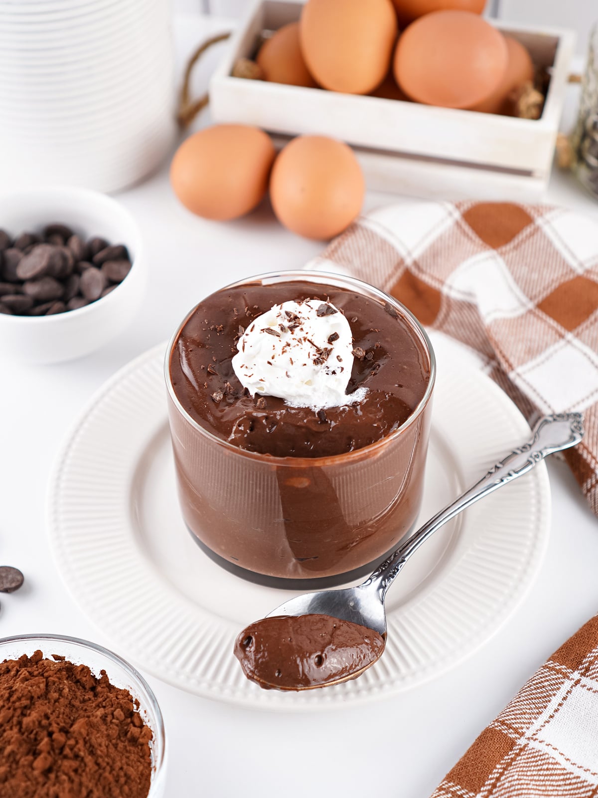Glass cup of rich chocolate hard-boiled egg pudding topped with whipped cream, with a spoonful served in front.