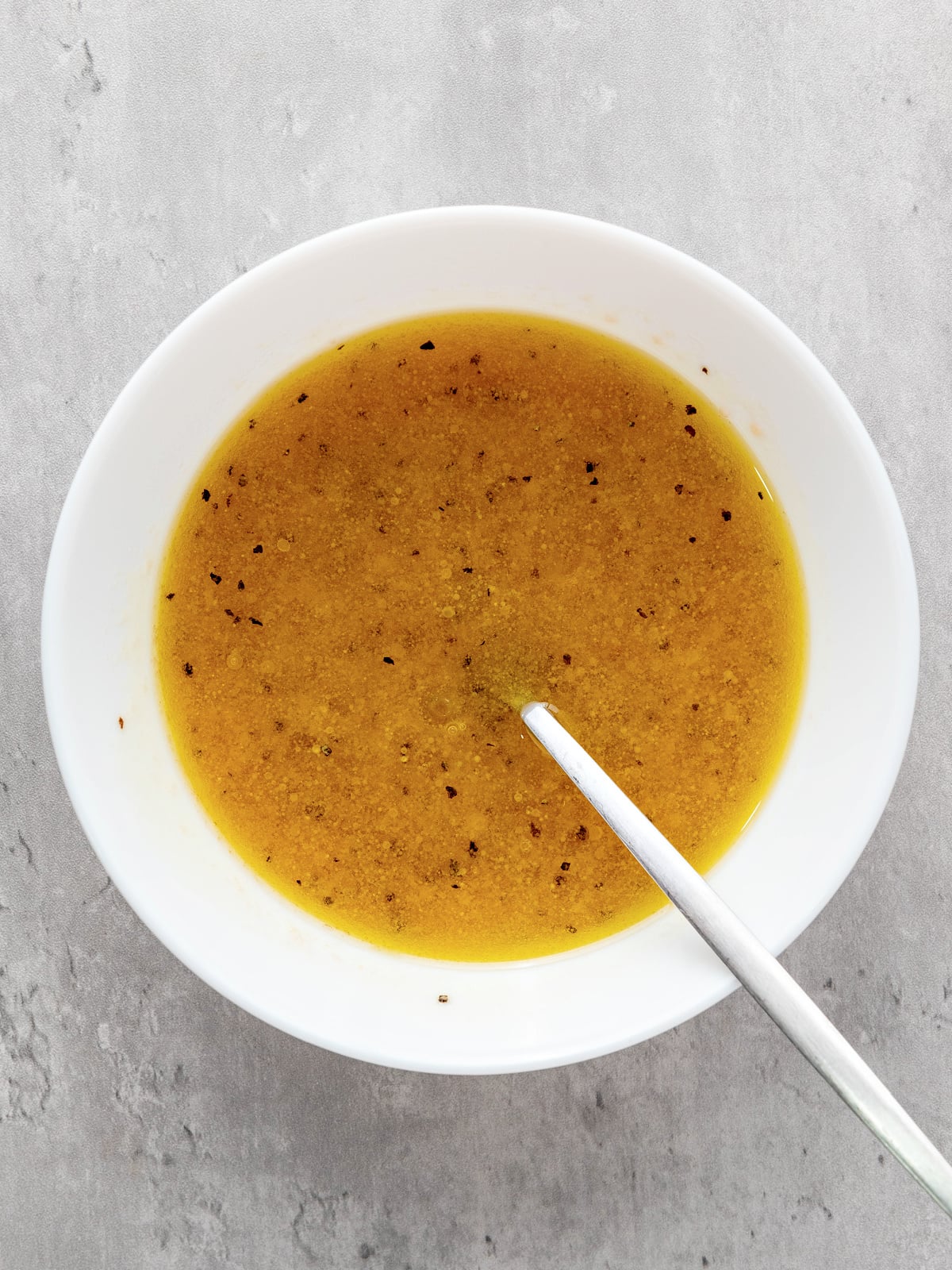 Homemade vinaigrette for panzanella salad made with olive oil, red wine vinegar, Dijon mustard, garlic, and seasonings in a white bowl.