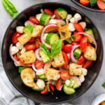 Italian bread salad with cherry tomatoes, cucumbers, mozzarella, red onion, basil, and toasted ciabatta cubes in a black bowl, viewed from above.
