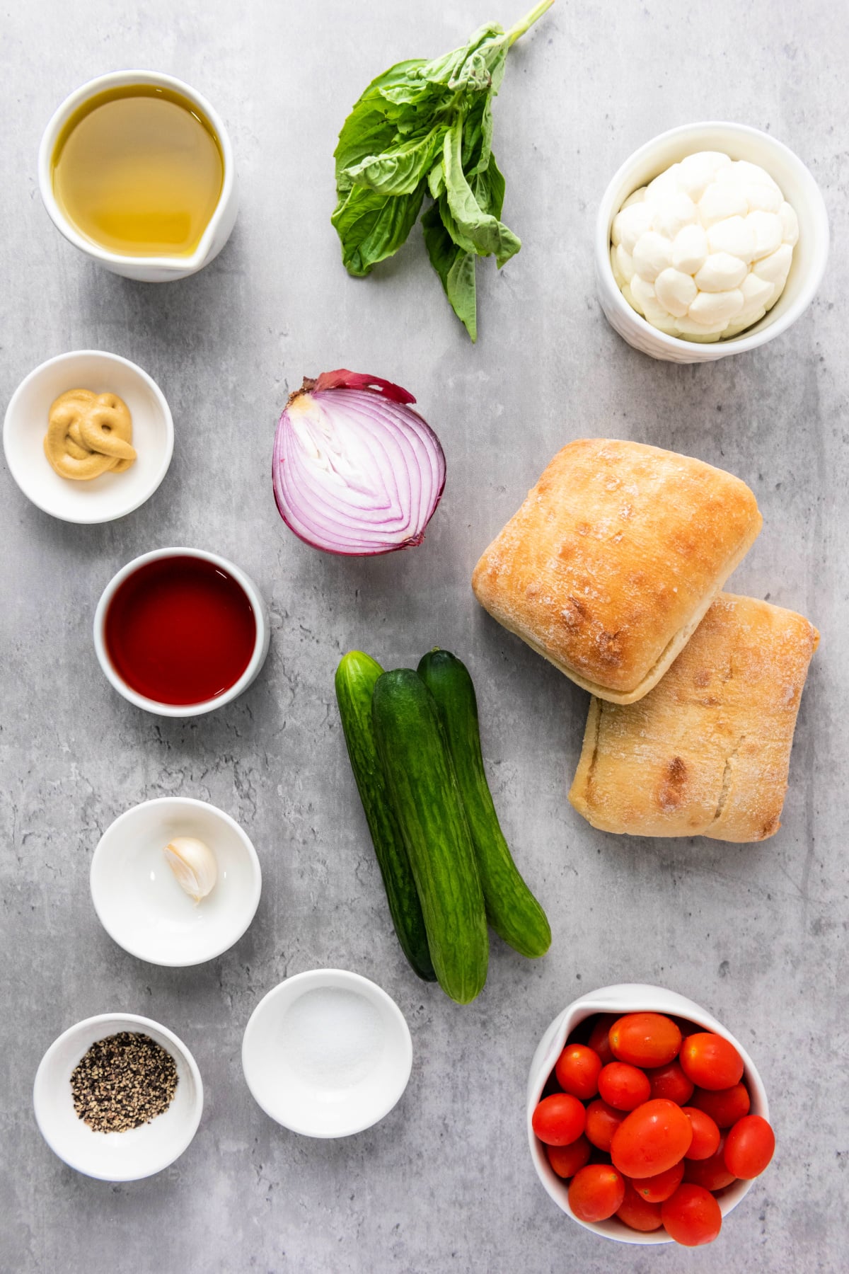 Ingredients for panzanella salad including ciabatta bread, cherry tomatoes, cucumbers, red onion, basil, mozzarella, olive oil, vinegar, garlic, Dijon mustard, salt, and pepper.