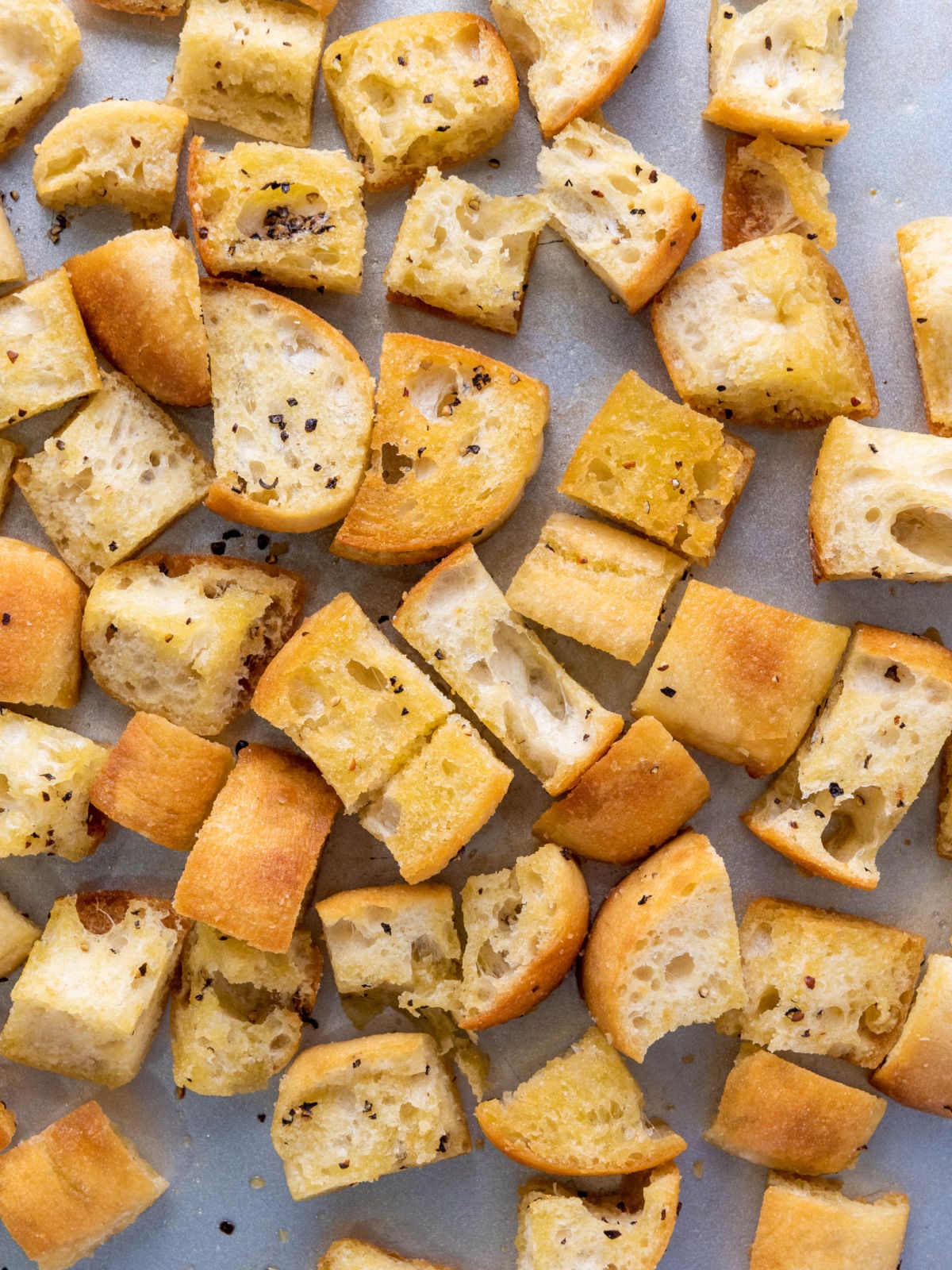 Golden toasted ciabatta bread cubes seasoned with olive oil and black pepper on a parchment-lined baking sheet.