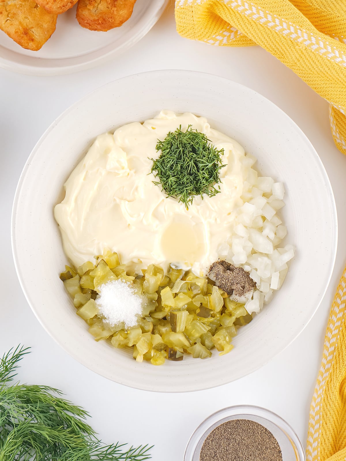 Bowl filled with tartar sauce ingredients before mixing, including mayonnaise, pickles, onion, dill, lemon juice, and seasonings.