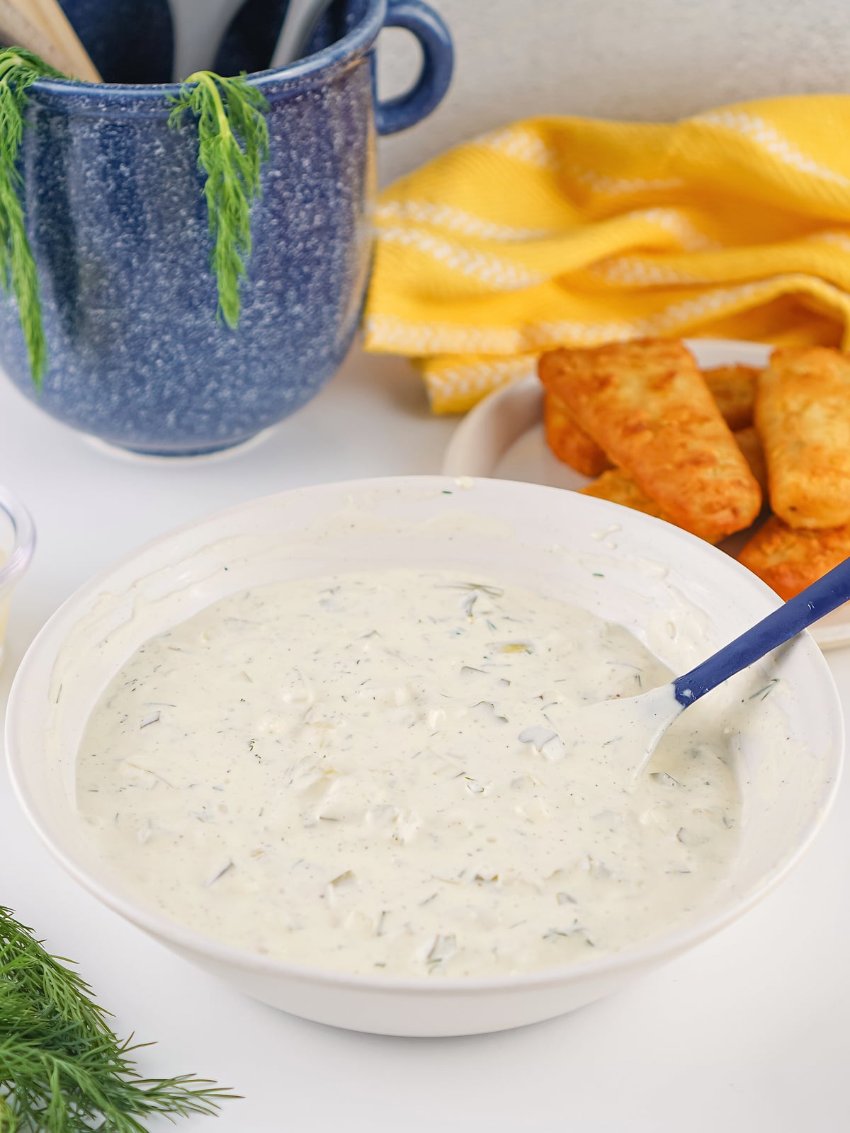 Bowl of homemade tartar sauce mixed with dill and chopped pickles, ready to serve with crispy fish sticks in the background.