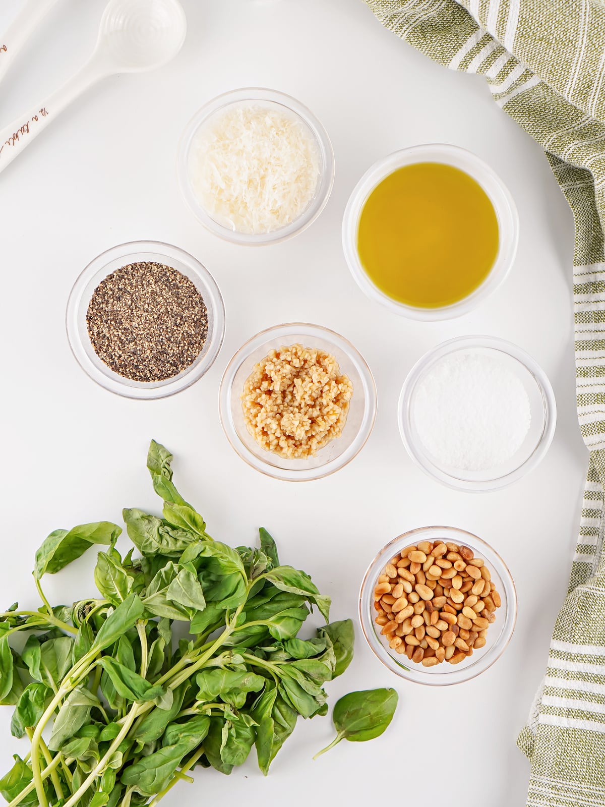 Fresh basil, toasted pine nuts, Parmesan cheese, garlic, olive oil, salt, and pepper arranged for making homemade pesto.