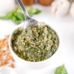 Spoonful of homemade basil pesto over a bowl of freshly blended pesto made with basil, Parmesan, garlic, and toasted pine nuts.