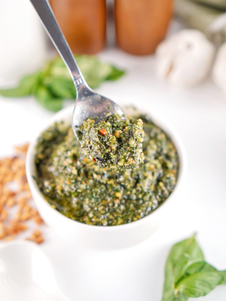 Spoonful of homemade basil pesto over a bowl of freshly blended pesto made with basil, Parmesan, garlic, and toasted pine nuts.