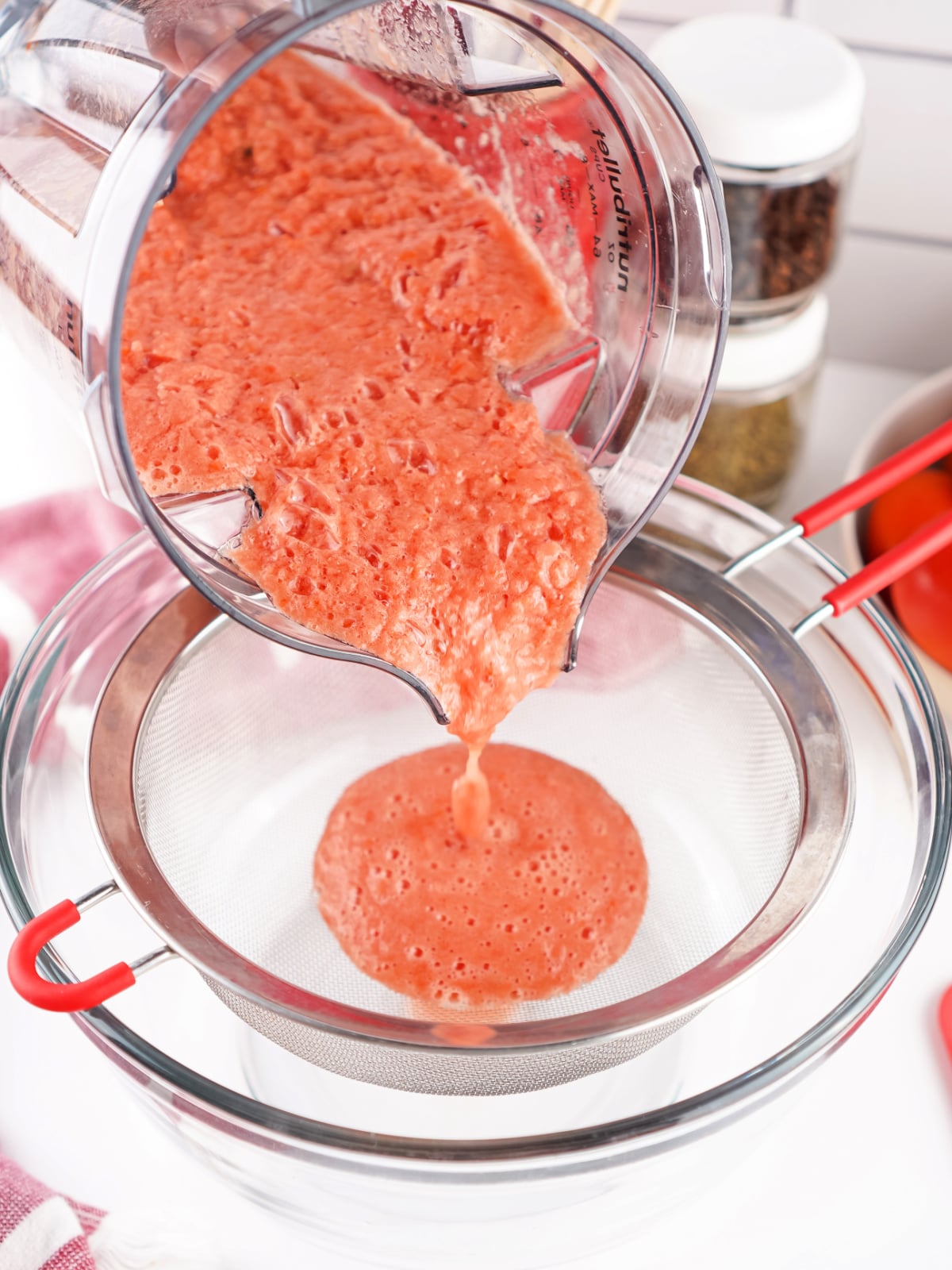 Blended tomatoes being poured through a fine mesh sieve to separate excess liquid before cooking.