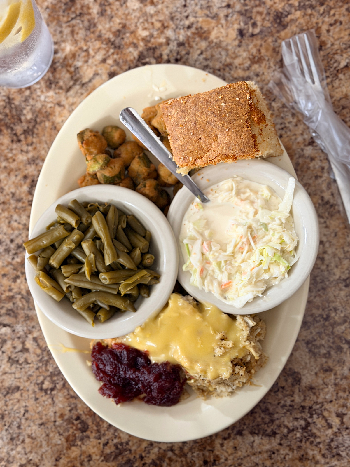 Southern chicken lunch with green beans, fried okra, coleslaw, cranberry sauce, and a large piece of cornbread.