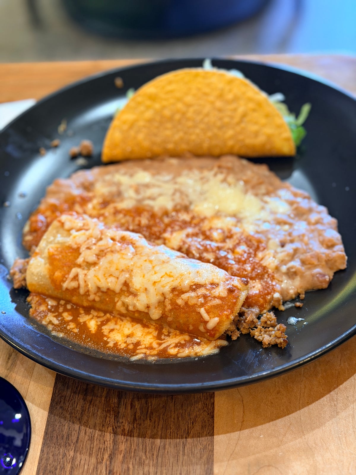 Mexican combination plate with a cheese-topped enchilada, refried beans, and a crispy taco.