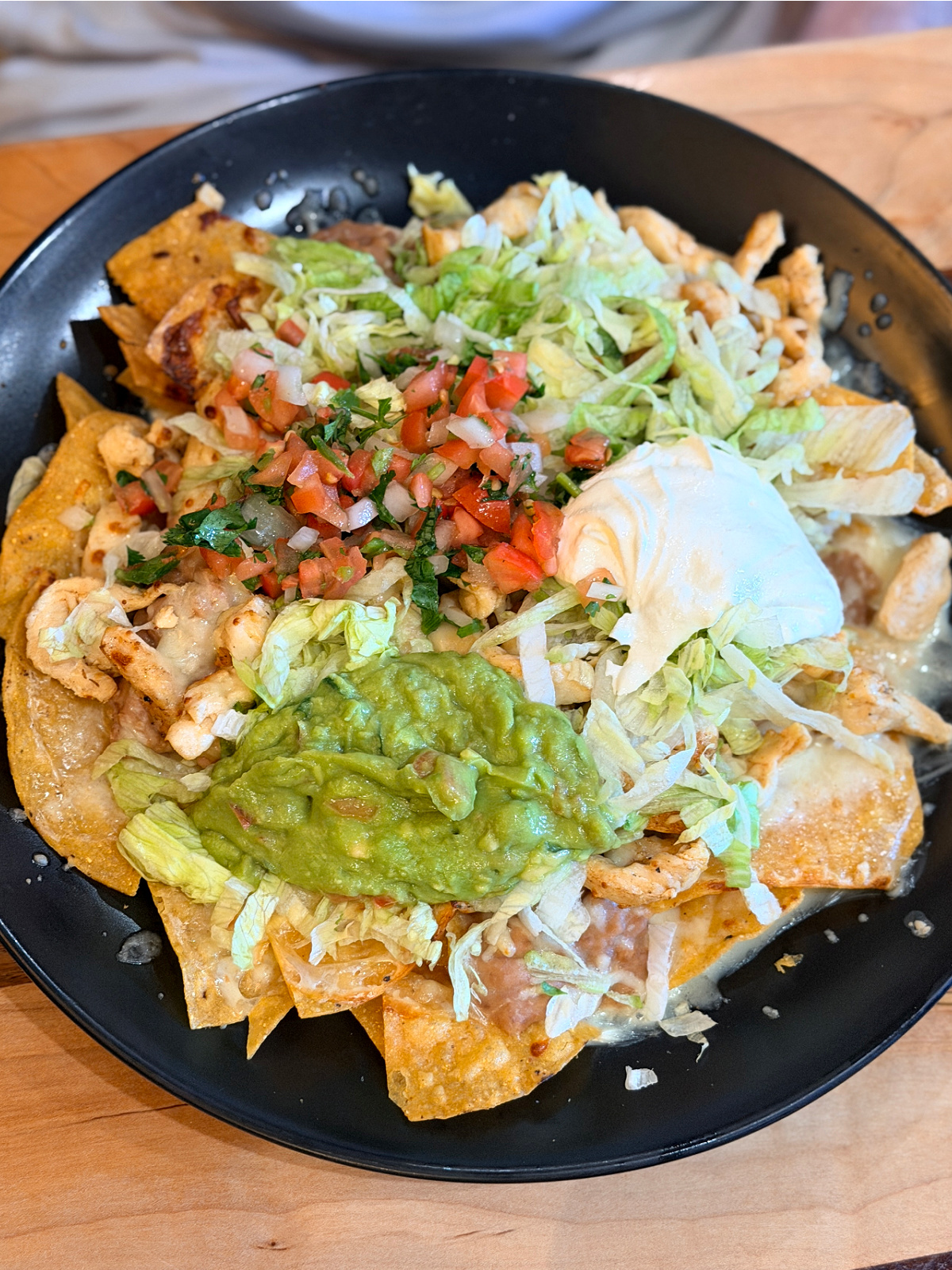 Chicken nachos topped with lettuce, pico de gallo, guacamole, sour cream, and cheese.