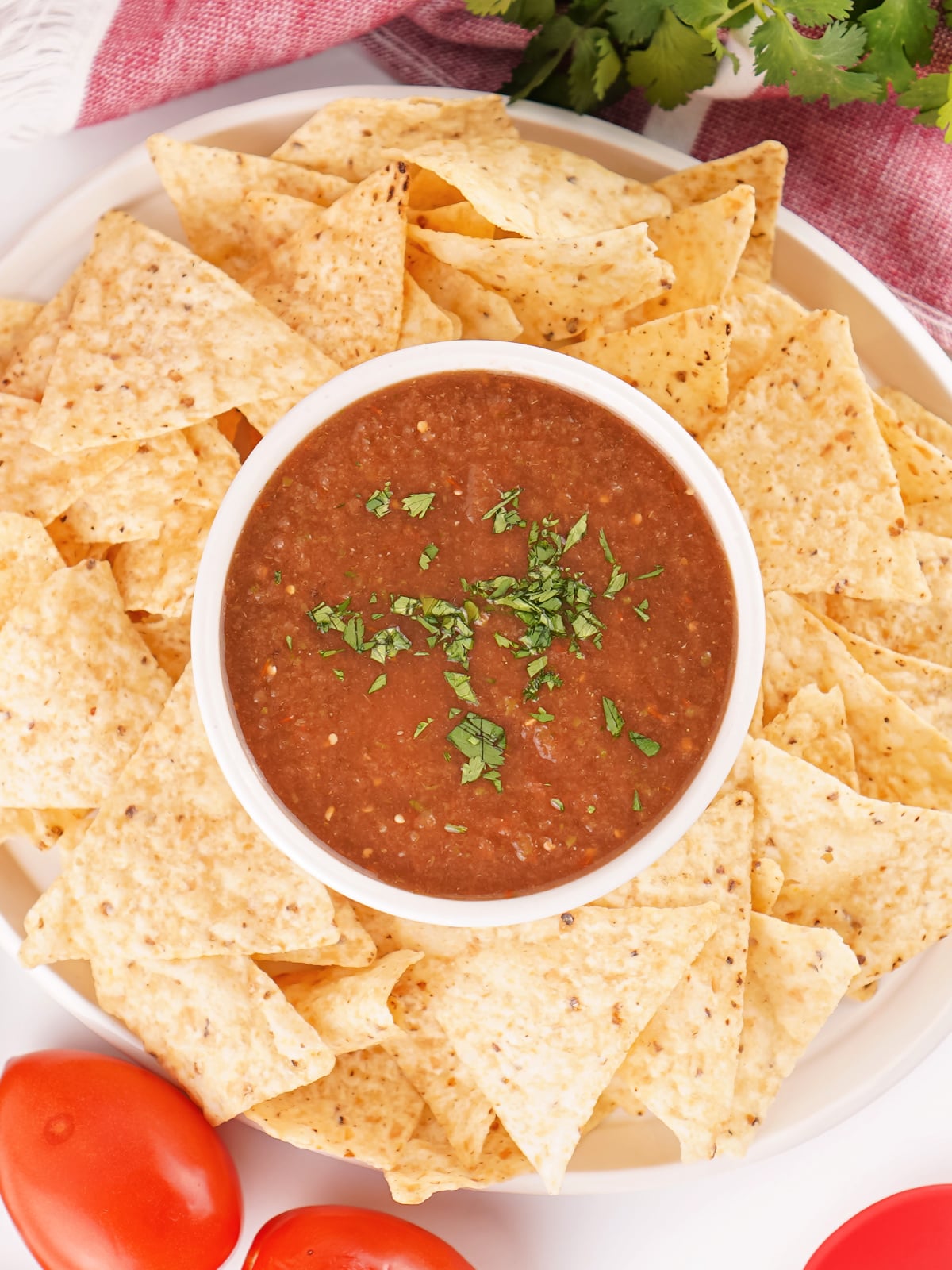 Restaurant style salsa garnished with fresh cilantro served in a white bowl surrounded by tortilla chips on a platter.