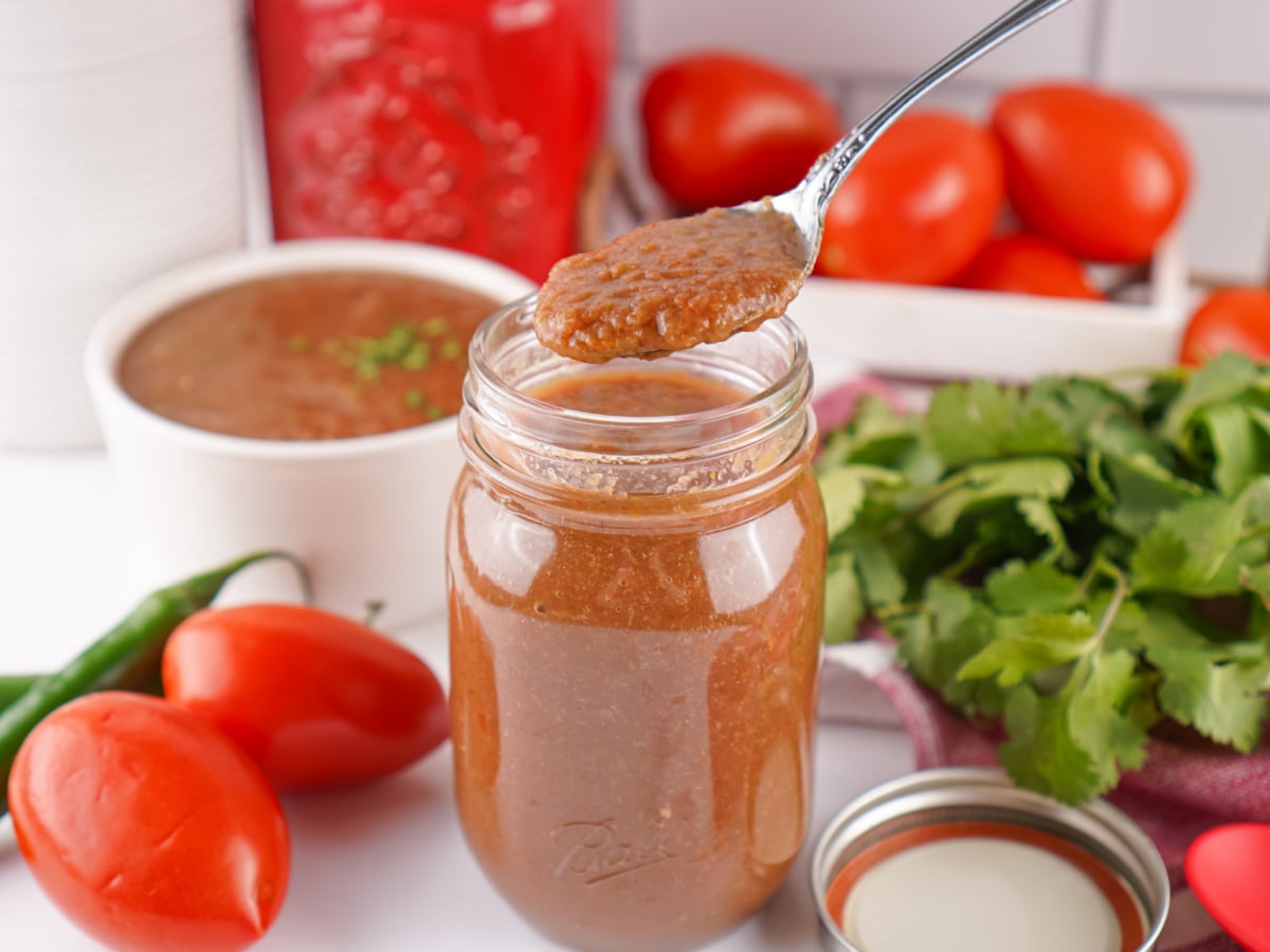 Spoon lifting smooth restaurant style salsa above a mason jar filled with fresh homemade salsa.