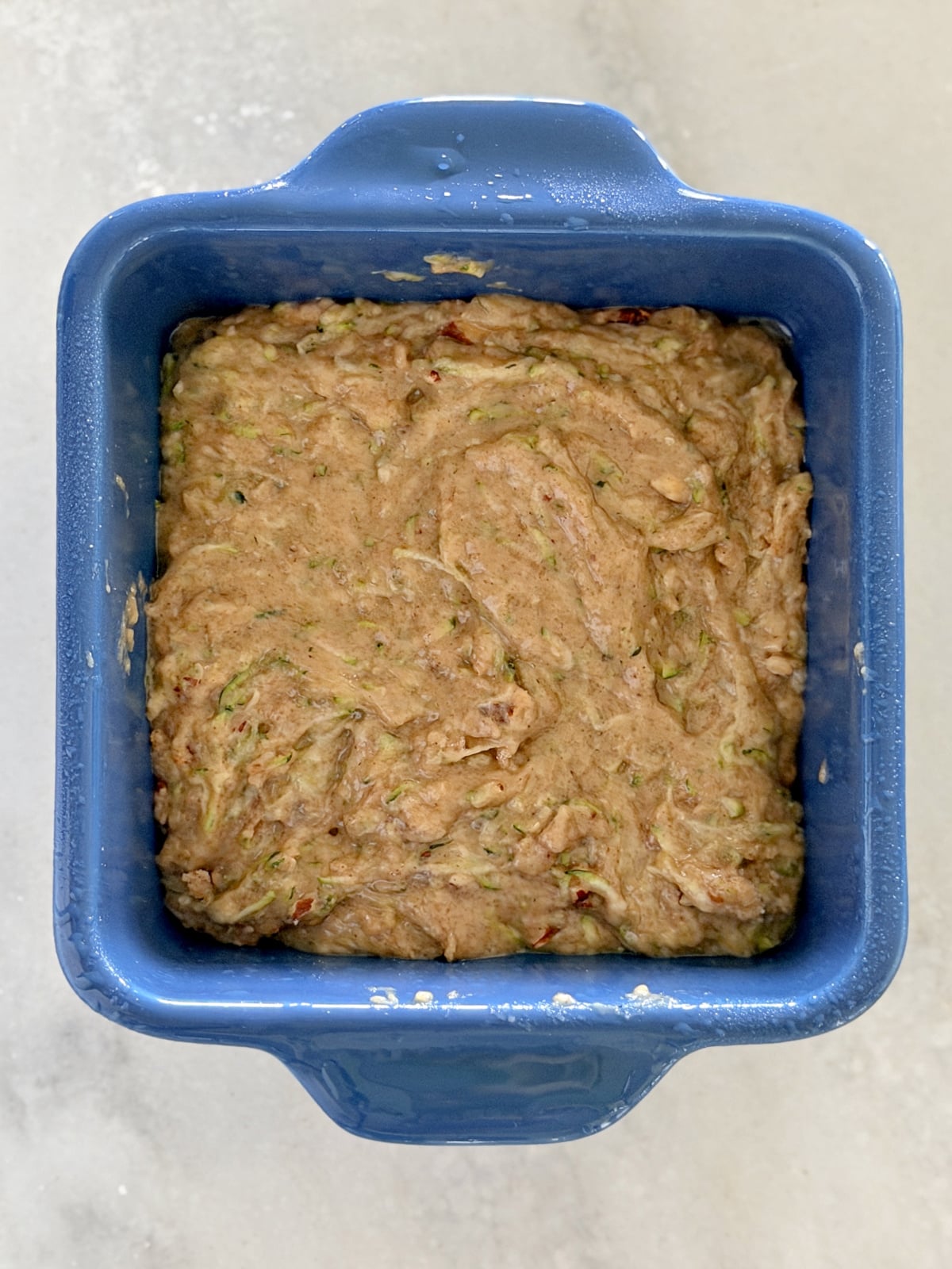 Zucchini bread batter spread in a small blue ceramic baking dish.
