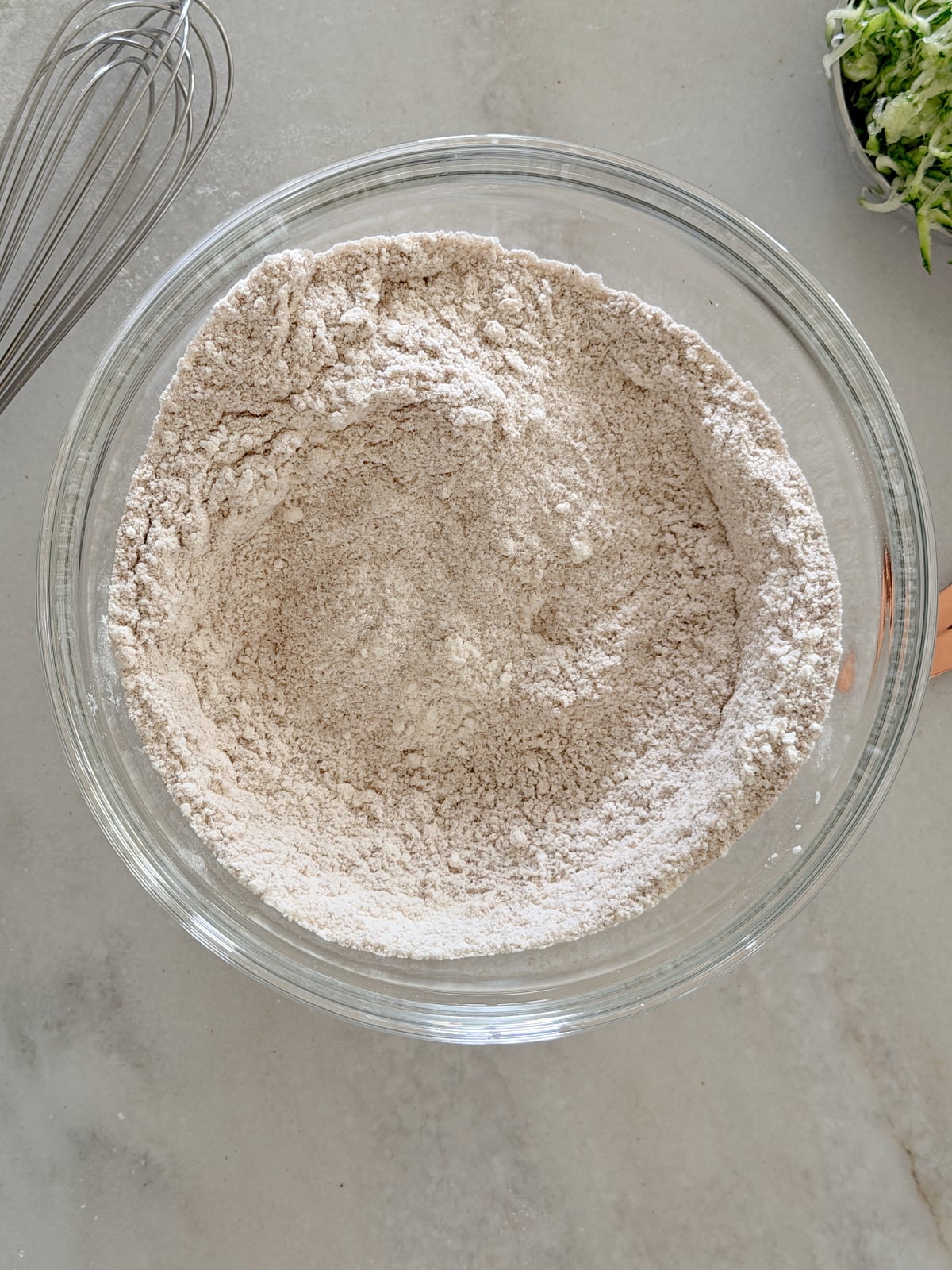 Dry ingredients for zucchini bread combined in a clear glass mixing bowl.