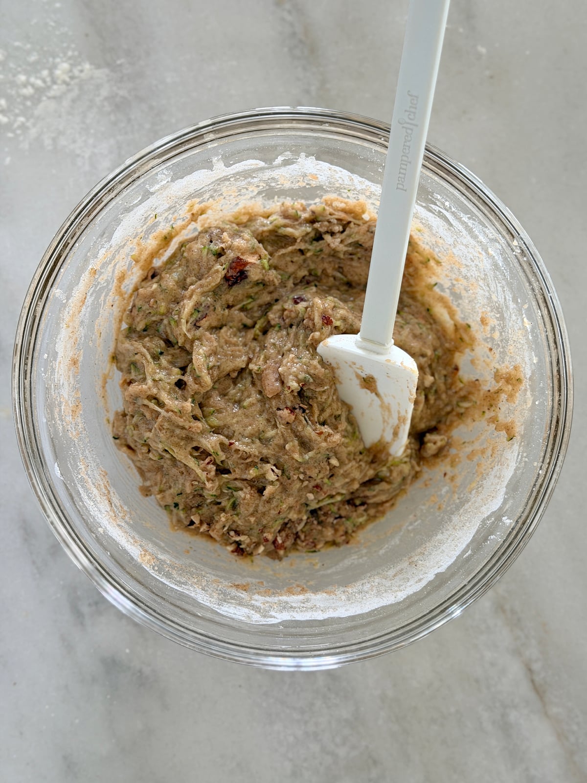 Thick zucchini bread batter being mixed with a spatula in a glass bowl.