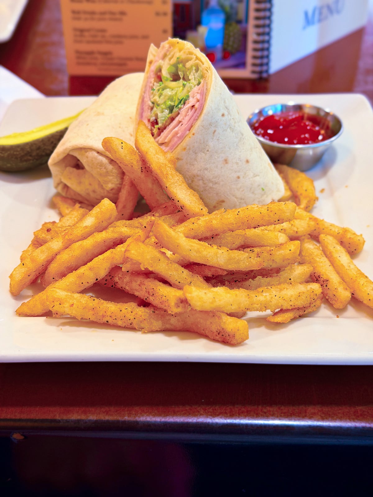 Sliced club wrap filled with turkey, ham, lettuce, and cheese, served with seasoned fries and ketchup.