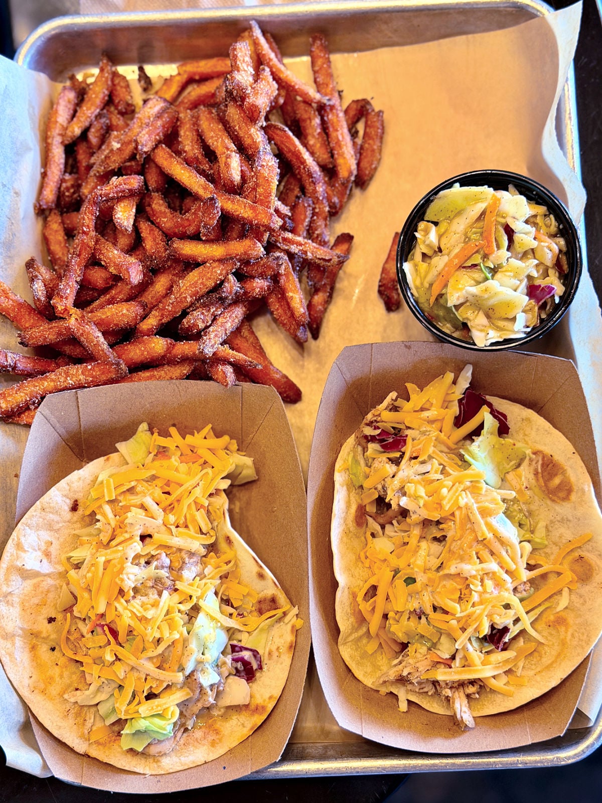 Two barbecue tacos topped with shredded cheese and slaw, served with fries and coleslaw.
